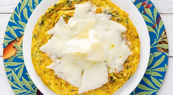 Frittata di bietole dorata e filante, servita su un piatto bianco con un sottobicchiere blu decorato con pesci e foglie.