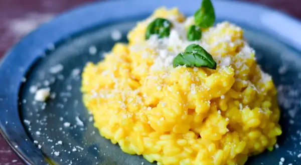 Pyszny, kremowy ryż do risotto, posypany parmezanem i udekorowany listkami bazylii, na niebieskim talerzu.