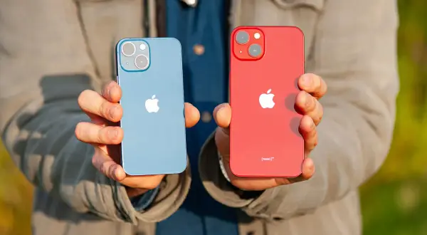 Dwie ręce trzymają dwa telefony: niebieski i czerwony iPhone 13 mini. Oba mają charakterystyczny aparat.