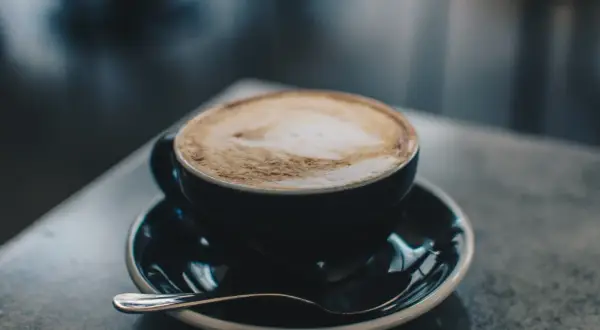 En kopp cappuccino med lattekonst, en av många italienska kaffesorter, står på ett fat med en sked.