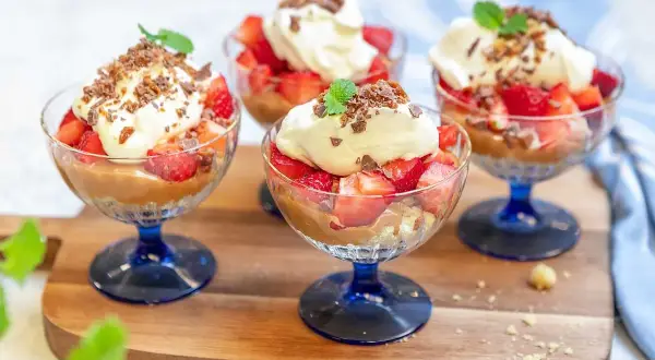 Fyra glas med jordgubbar, grädde och chokladsmulor. En härlig somrig dessert som ser otroligt god ut!