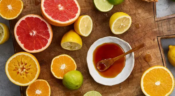 Färska citrusfrukter som apelsiner, grapefrukt och citroner, samt en skål med mörk vätska, antyder ingredienser för ett ponzu recept.