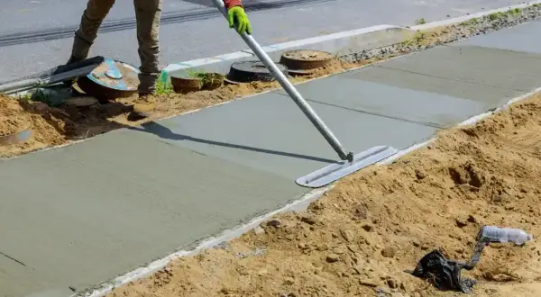 Robotnik wygładza świeży beton C20/25 na chodniku. Właściwe proporcje składników zapewniają trwałość.