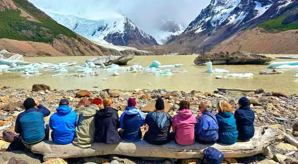 Gruppe sitzt auf Baumstamm vor Gletschersee mit Eisbergen. Tolle Eberhardt Travel Erfahrungen in Patagonien.