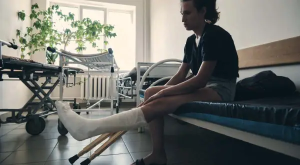Kobieta z nogą w gipsie i kulami czeka na rehabilitację po złamaniu nogi.