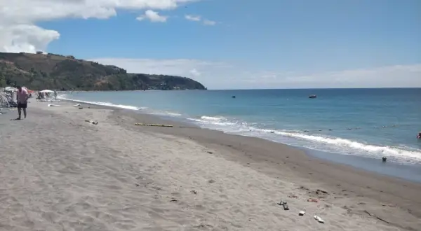 Plaża na wyspie Dominika z ciemnym piaskiem, turkusową wodą i zielonymi wzgórzami w tle.