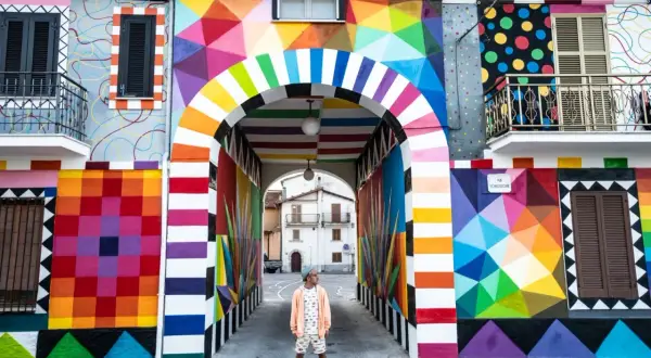 Un uomo in piedi sotto un arco colorato, un'esplosione di arte urbana che celebra l'Italia, patria della bellezza.