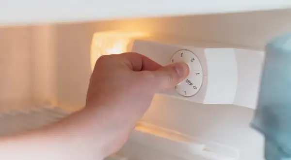 Main tenant ajuste la température d'un frigo. Le bouton est réglé sur 1, juste au-dessus de "STOP".