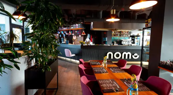 Elegancka restauracja z drewnianymi stołami, bordowymi krzesłami i barem z logo "nome".