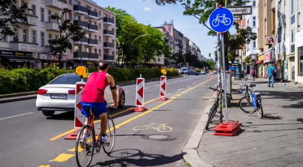 Ein Mann fährt auf einem pop-up Radweg in Berlin. Absperrungen markieren den Weg, der von Autos und Gebäuden gesäumt ist.