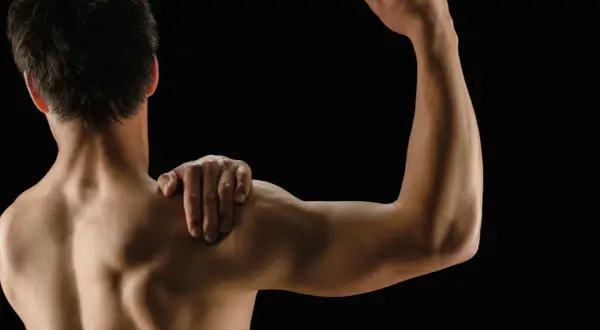 Mężczyzna z ręką na ramieniu, pokazujący umięśnione plecy i biceps. Białko po treningu wspiera regenerację mięśni.