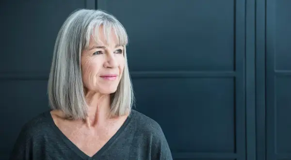 Een vrouw met grijs haar kijkt peinzend weg. Ze straalt een rustige kracht uit, wat kan passen bij de complexiteit van autisme bij vrouwen.