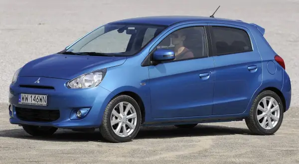 Niebieski Mitsubishi Mirage, idealny dla szukających bezawaryjnych samochodów do 20 tys. zł. Kobieta za kierownicą w okularach przeciwsłonecznych.