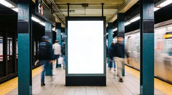 Gente se mueve rápido en el metro de Nueva York, pasando un anuncio en blanco.
