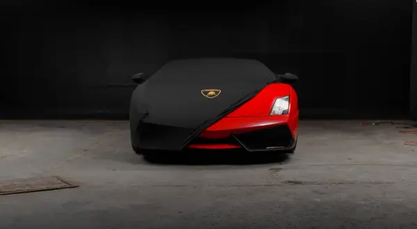 Czerwony supersamochód Lamborghini, być może najdroższe auto na świecie, częściowo przykryty czarnym pokrowcem z logo marki.