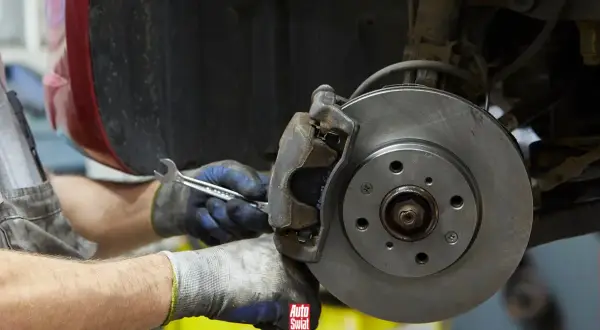 Mechanik w rękawicach dokręca śrubę przy budowie klocka hamulcowego.