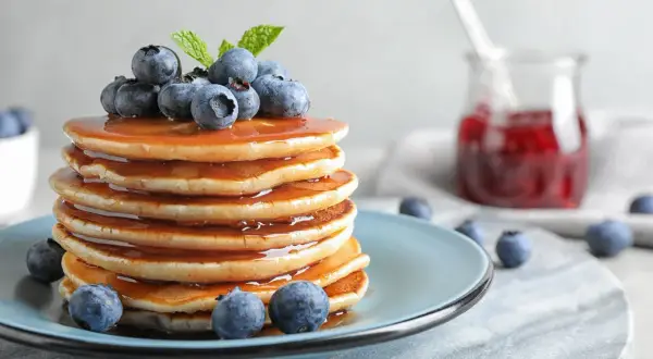 Stos puszystych naleśników polanych syropem, ozdobiony borówkami i miętą. Idealny przepis na pancake na pyszne śniadanie.