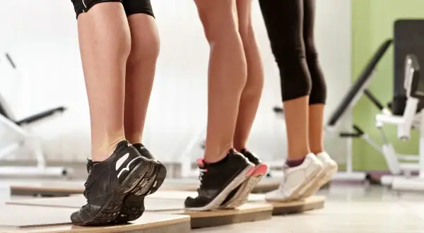 Tre donne eseguono un **calf raise** in palestra, sollevando i talloni per allenare i polpacci.