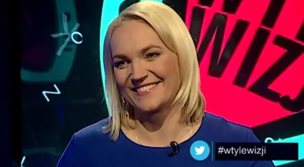 Uśmiechnięta blondynka w niebieskiej sukience. W tle wizji prowadzący, litery i cyfry.