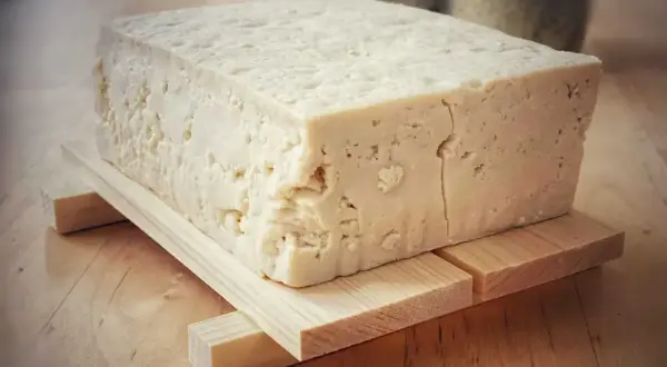 Duży blok domowego, białego tofu na drewnianej podstawce.