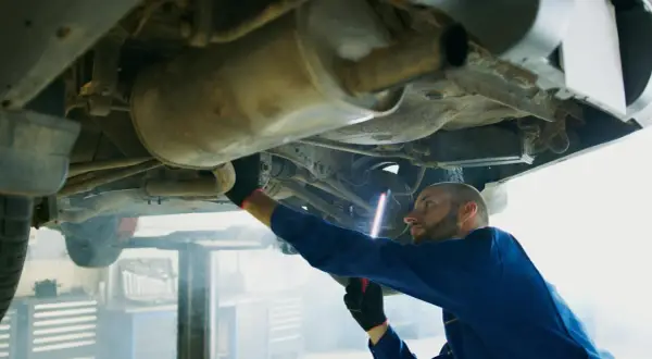 Mechanik w niebieskim kombinezonie oświetla latarką p0420 podwozie samochodu.