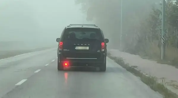 Ciemny van Dodge jedzie we mgle, włączone światła przeciwmgielne tylne poprawiają widoczność.