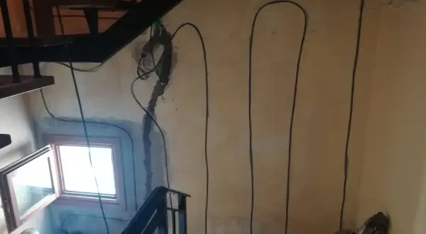Lavori in corso per l'isolamento pilastri: cavi neri corrono lungo la parete accanto a una scala e una finestra.
