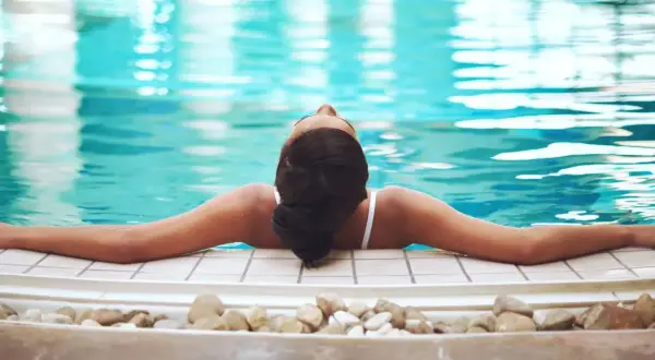 Avslappnad kvinna njuter av ett spa i Tyskland, med armarna utsträckta över kanten av en turkos pool.