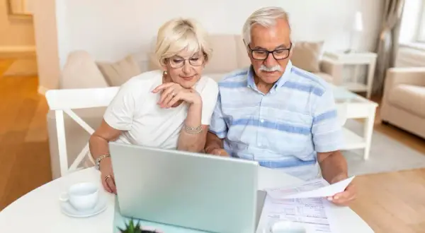 Para seniorów analizuje dokumenty przy laptopie, zastanawiając się, czy emeryci częściej wygrywają w loteriach pożyczkowych skierowanych do seniorów.