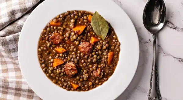 Un plato de lentejas estofadas con trozos de zanahoria y chorizo, decorado con una hoja de laurel.
