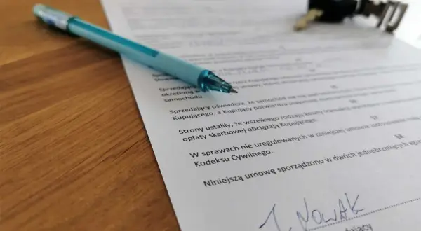 Długopis i kluczyki leżą na dokumencie, który pomoże Ci dowiedzieć się, jak spisać umowę kupna-sprzedaży samochodu.