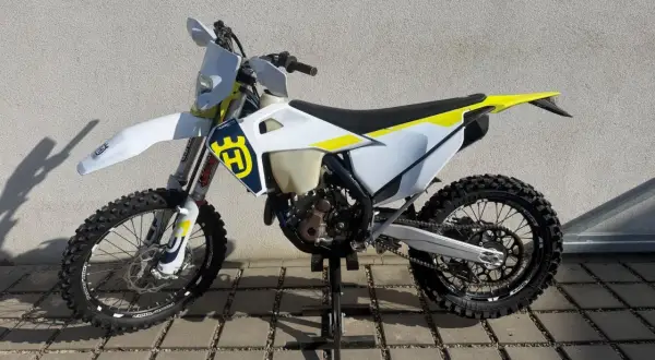 Motocykl Husqvarna WRE 125 na stojaku, biało-żółty, z logo Husqvarna.