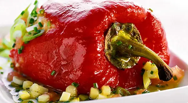 En fylld, röd paprika serveras på en vit tallrik med en sallad av tärnad paprika och örter. Ett läckert recept med grillad paprika på burk.