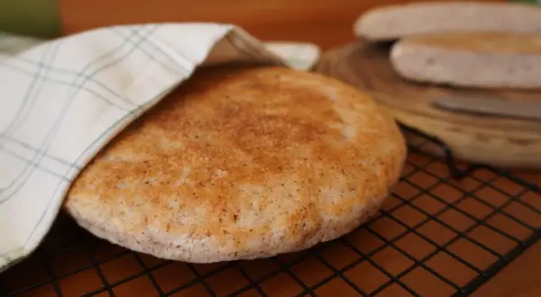 Pan de arroz redondo y dorado, cubierto parcialmente con un paño a cuadros, sobre una rejilla.
