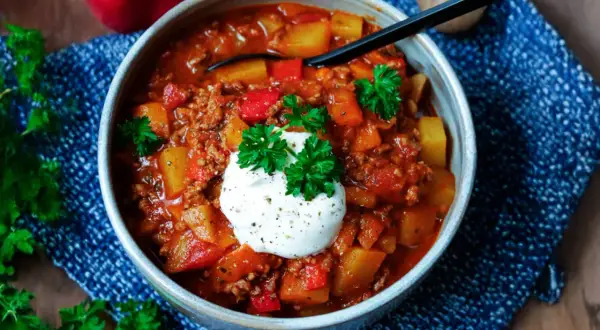 Herzhaftes Bauerntopf Rezept mit Hackfleisch, Kartoffeln und Paprika, garniert mit einem Klecks Sauerrahm und Petersilie.