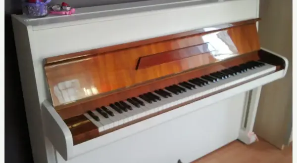 Białe pianino z drewnianymi elementami. Zastanawiasz się, ile kosztuje strojenie pianina?
