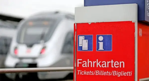 Roter Fahrkartenautomat am Bahnhof. Ein Zug fährt vorbei. Wann am besten Bahntickets buchen? Hier gibt es Infos.