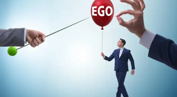 Mężczyzna z balonem "EGO" w ręku, symbolizujący cechy narcyza, zagrożony przez szpilkę.