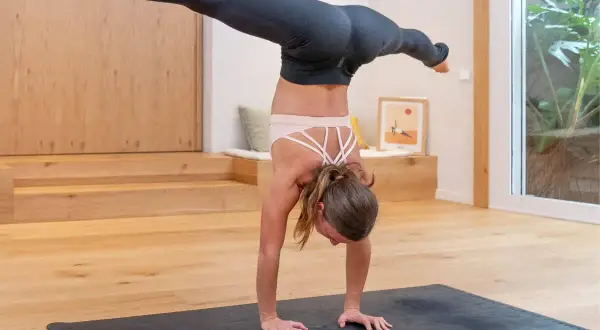 Mujer en postura del arbol yoga, con piernas extendidas en el aire, sobre una esterilla en un estudio luminoso.