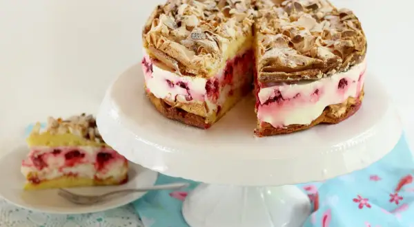 Himmlische Torte mit Baiser, Mandeln und Himbeercreme. Ein Stück ist bereits auf einem Teller angerichtet.