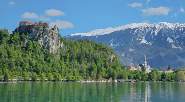 Blick auf die Burg von Bled über dem smaragdgrünen See, mit schneebedeckten Bergen im Hintergrund.