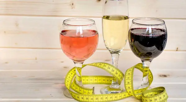 Trzy kieliszki z winem (różowym, białym, czerwonym) i miarka krawiecka. Zastanawiasz się, ile kcal ma pół litra wódki?