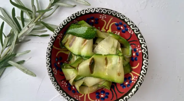 Gegrillte Zucchinibänder in einer bunten Schale mit Rosmarinzweig.