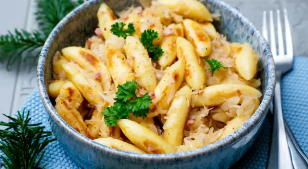 Herzhafte Bubespitzle mit Sauerkraut und Speck, garniert mit Petersilie, in einer blauen Schüssel.