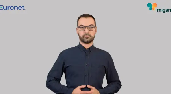 Mężczyzna w okularach i granatowej koszuli, z dłońmi złożonymi na brzuchu. Widoczne logo Euronet i Migam. Proces euronet rejestracja id.