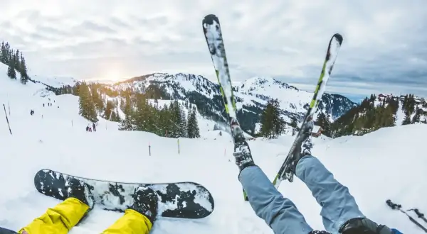 Narciarz i snowboardzista odpoczywają na stoku. Zastanawiasz się, co bardziej obciąża kolana: narty czy snowboard? Góry i słońce zachęcają do jazdy.