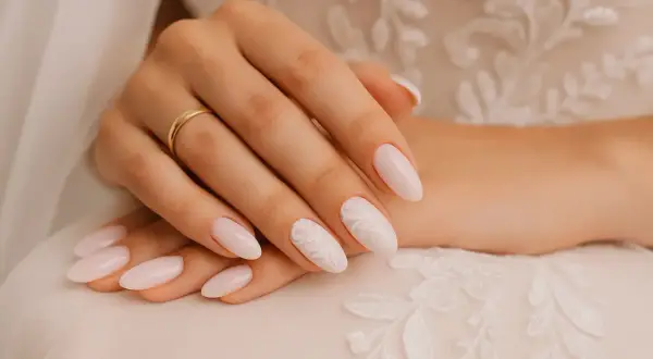 Mains d'une mariée aux ongles pastel ornés de dentelle blanche, parfaits pour un mariage.