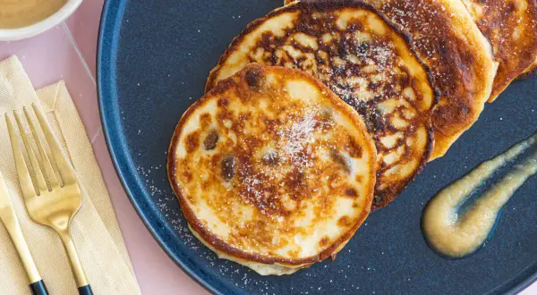 Goldene quarkkeulchen ohne kartoffeln, bestreut mit Zucker, serviert mit Apfelmus auf einem dunklen Teller.