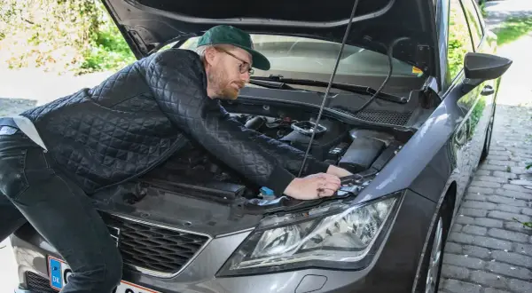 Man med keps och glasögon böjer sig över motorhuven för att byta halogenlampa.