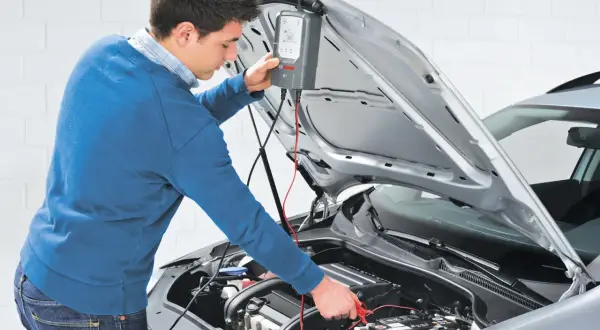 Uomo effettua manutenzione batteria auto con un tester Bosch.